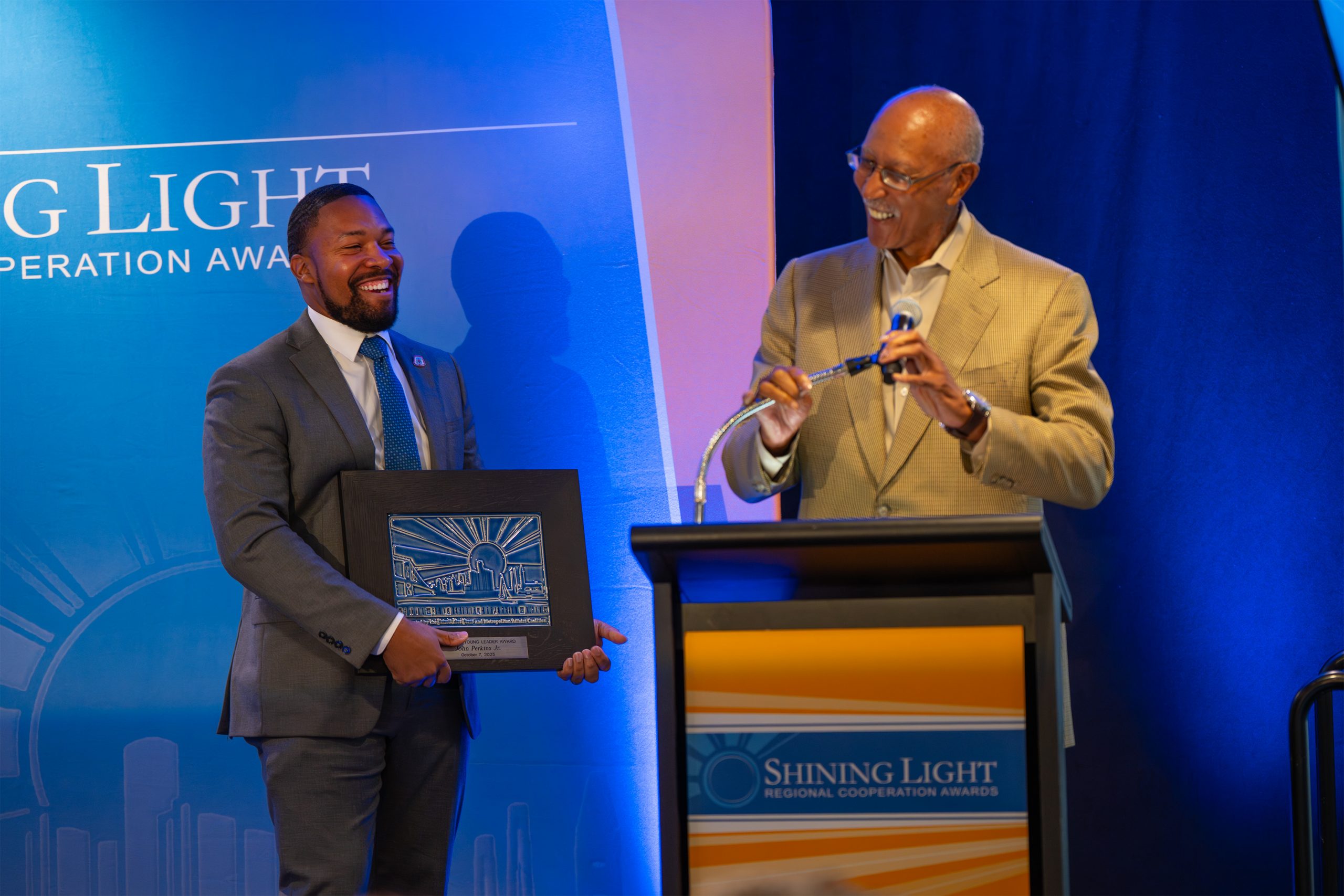 Elevated image of two men at the Shining Light Regional Cooperation Awards ceremony, one receiving an award and the other presenting it, showcasing recognition for leadership and community impact.