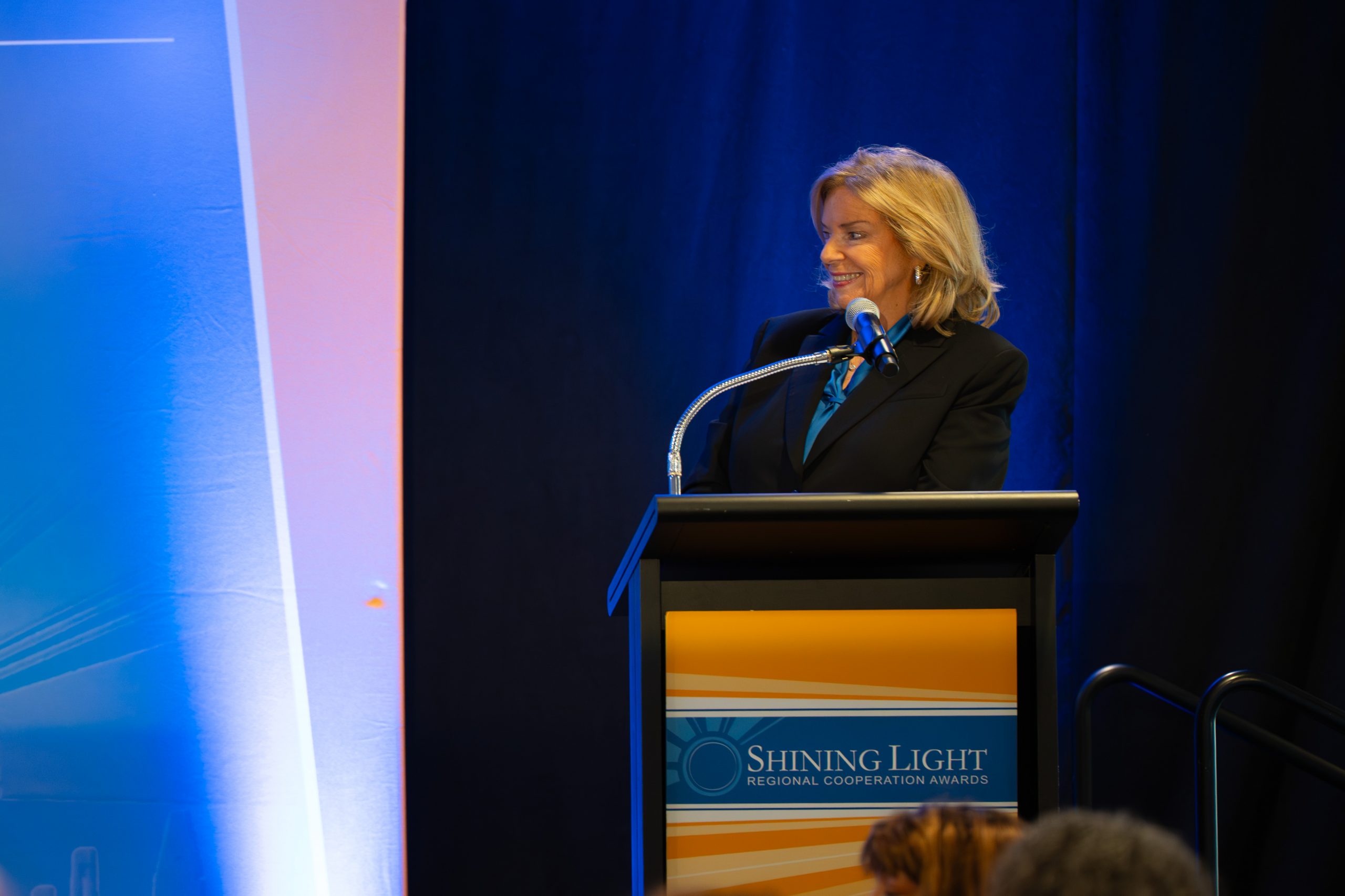 Empowered woman speaking at the Shining Light Regional Cooperation Awards ceremony, emphasizing community recognition and leadership.