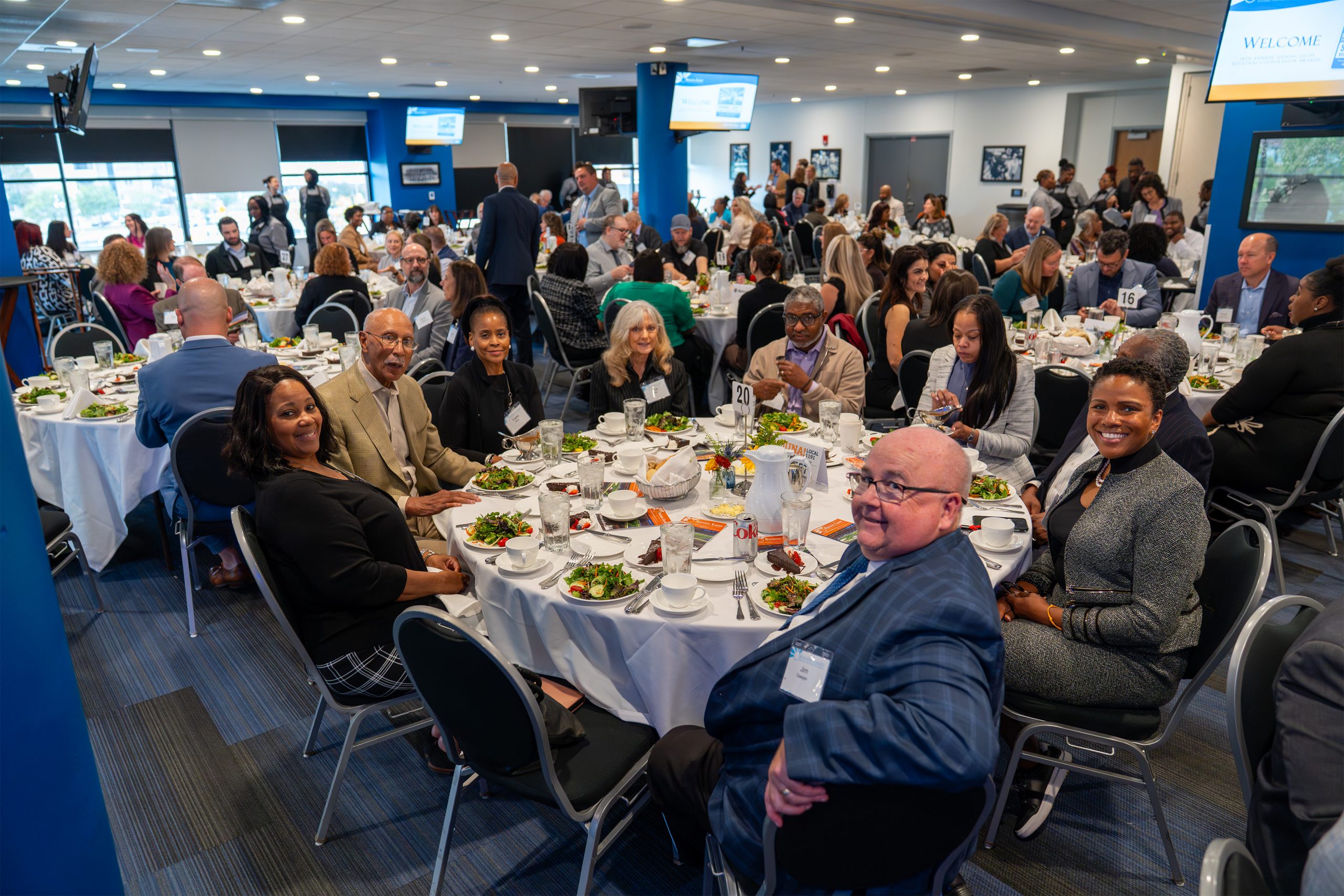Formal awards banquet at Shining Light event, attendees enjoying dinner, networking, and celebrating excellence in a modern conference room with multiple screens displaying event information.